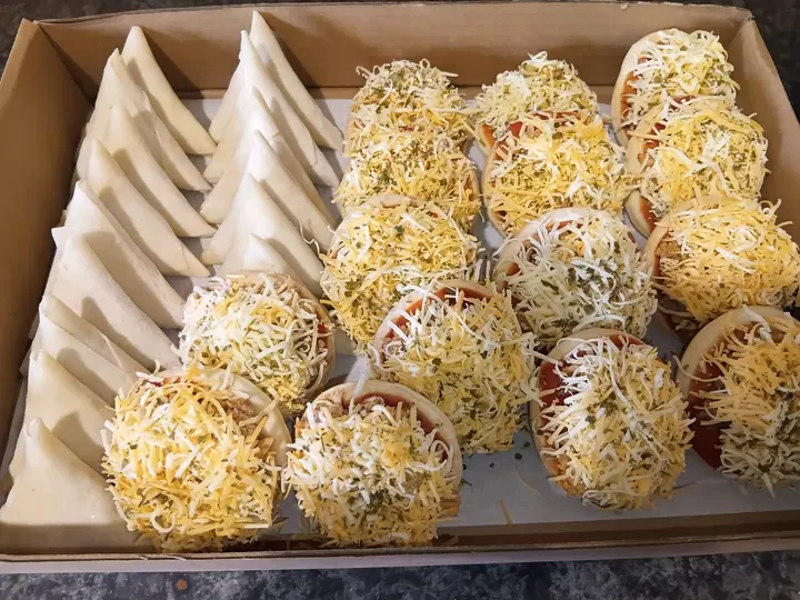 Tray of unbaked samoosa pastries and mini pizzas topped with grated cheese