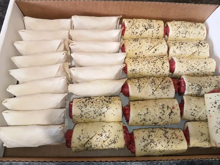 Uncooked spring rolls and sausage rolls packed in a box